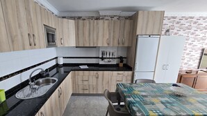 A compact kitchen with wooden cabinets, a black countertop, a sink, a microwave, and a refrigerator.