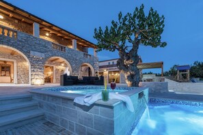 A stone building with a swimming pool, outdoor seating, and a tree.