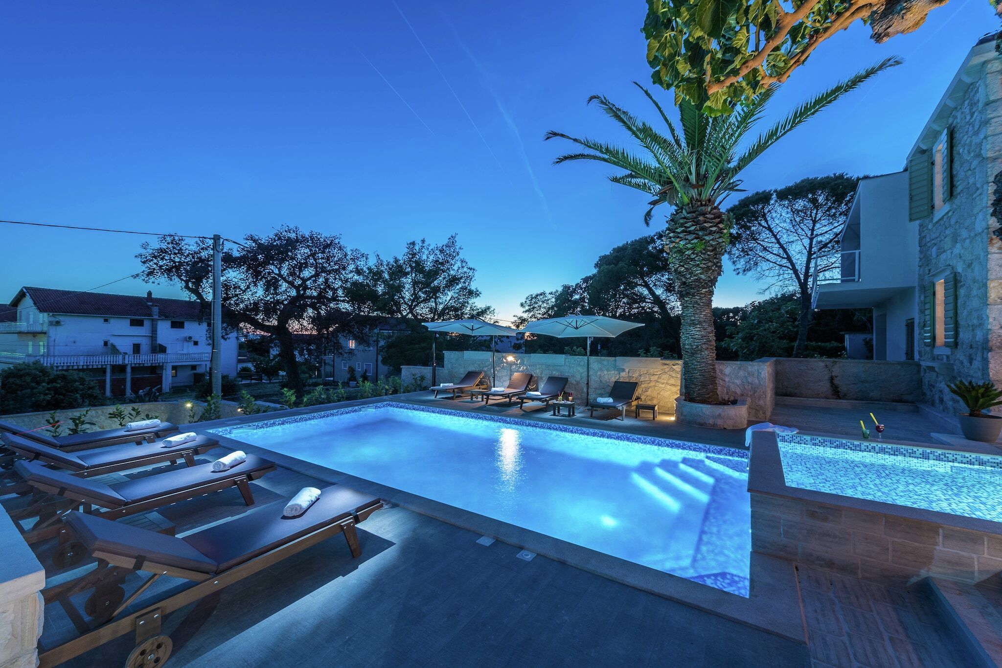 A swimming pool with lounge chairs and umbrellas, surrounded by trees and buildings.