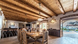 Un grand espace dédié à la salle à manger, avec une table et des chaises en bois, une cuisine en arrière-plan et une vue sur une piscine.