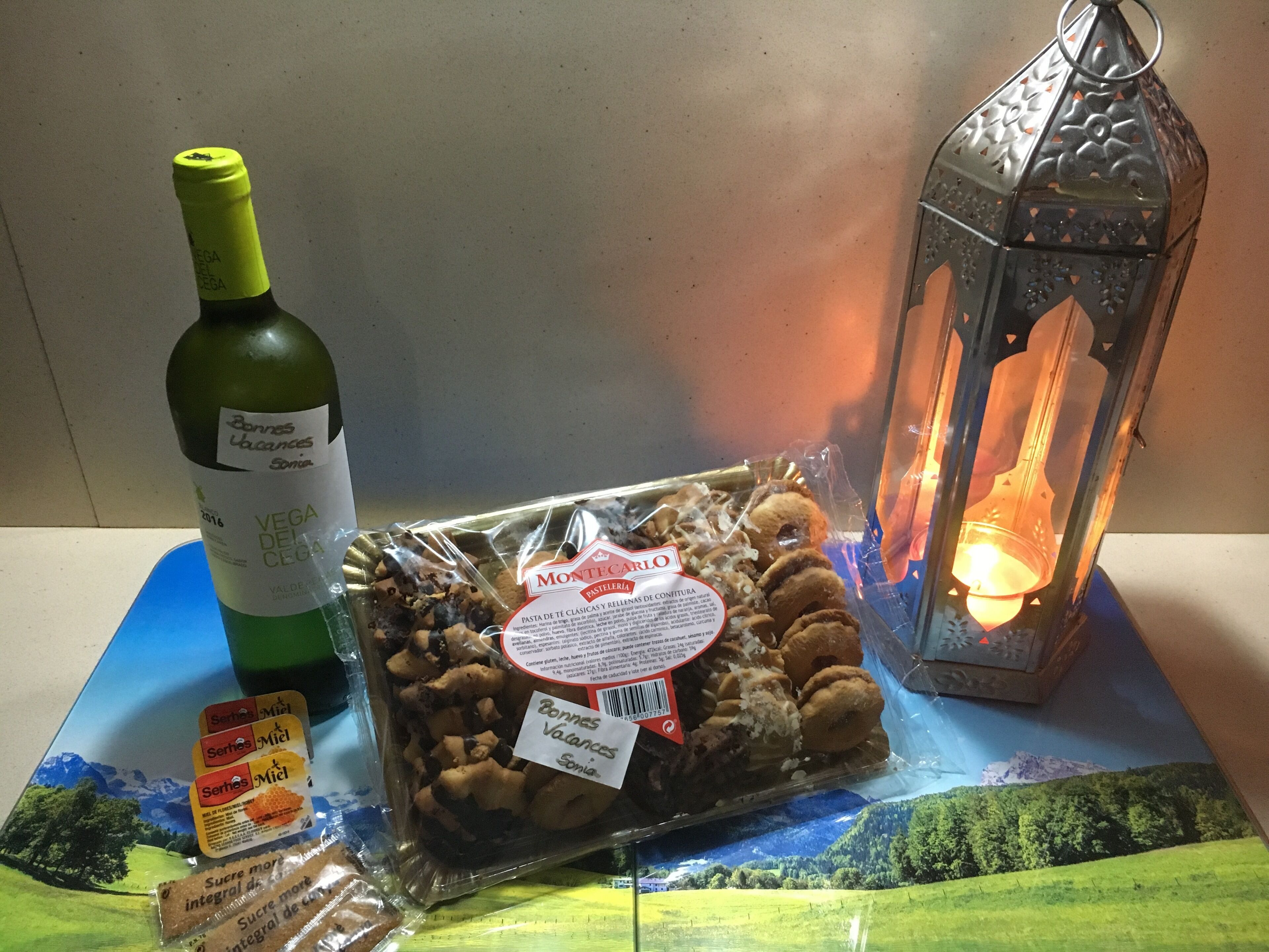 A bottle of wine, a package of cookies, and a lit lantern on a table.