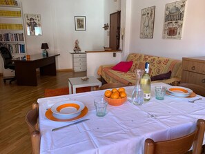 Un salon chaleureux avec une table à manger dressée pour deux personnes, une bibliothèque, un canapé et un petit bureau.