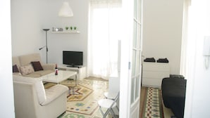 Un salon avec un canapé, une table basse, un téléviseur et une petite étagère ornée de plantes.