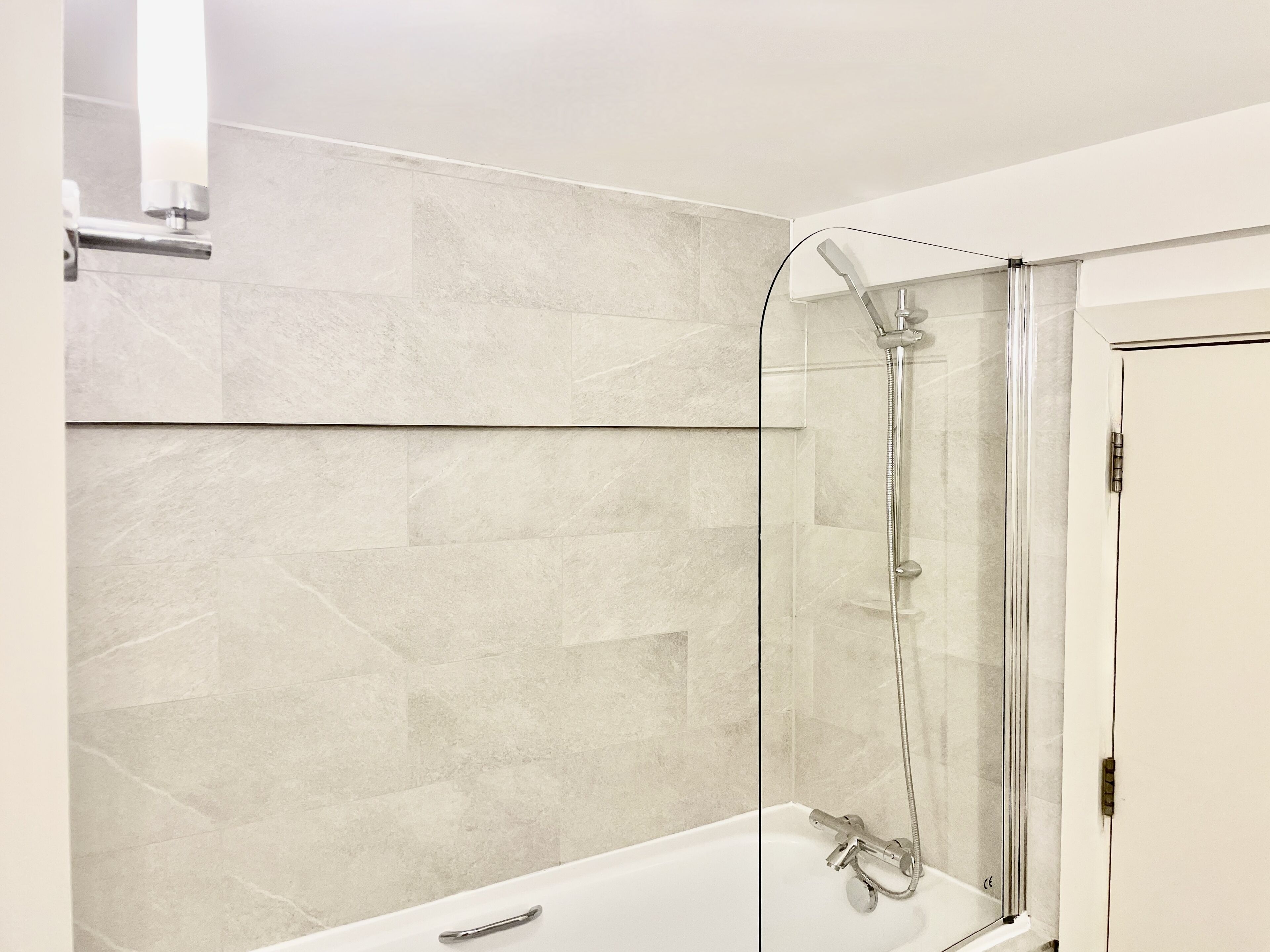 Une salle de bain moderne avec une douche à parois de verre, une baignoire blanche et un mur recouvert de carreaux.