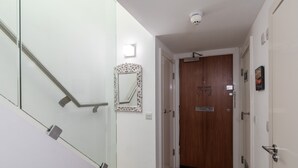 A hallway with a wooden door, a glass railing, and a mirror on the wall. - A Stylish 2 Bed, 2 Bath London Apartment (London)