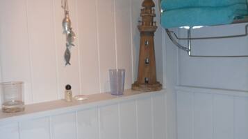 Casa de banho com sanita, uma prateleira com uma toalha, um copo e um objeto decorativo pequeno.
