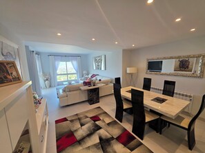Una sala de estar moderna con un sofá, mesa de comedor, sillas y vista al exterior.
