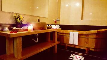 A wooden bathtub with a towel, a mirror, a candle, and toiletries on a wooden shelf.