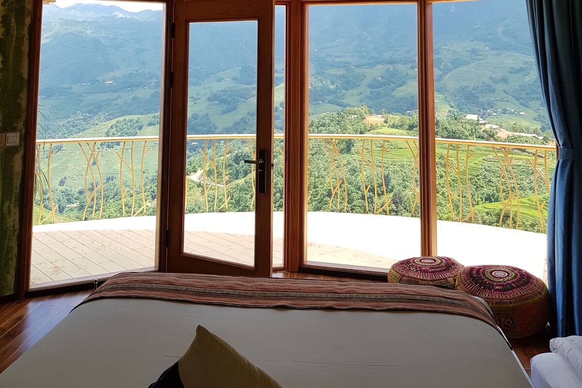 Une chambre dotée d’un grand lit, offrant une vue sur des collines verdoyantes, et dont le plafond est orné de motifs géométriques.