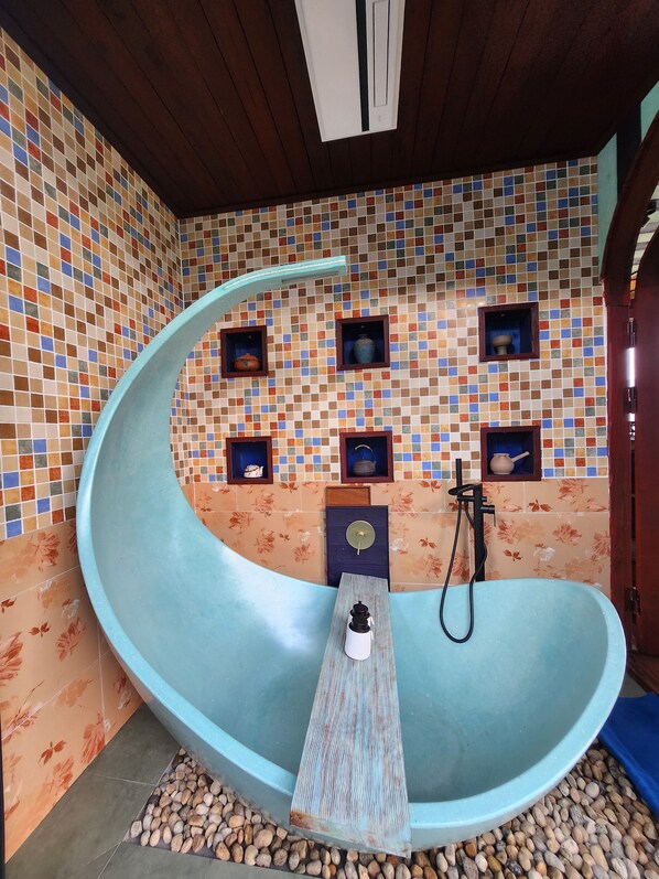 Eine Badausstattung mit einer gebogenen Badewanne, einer Holzbank, einer Duschbrause und dekorativen Fliesen an den Wänden.
