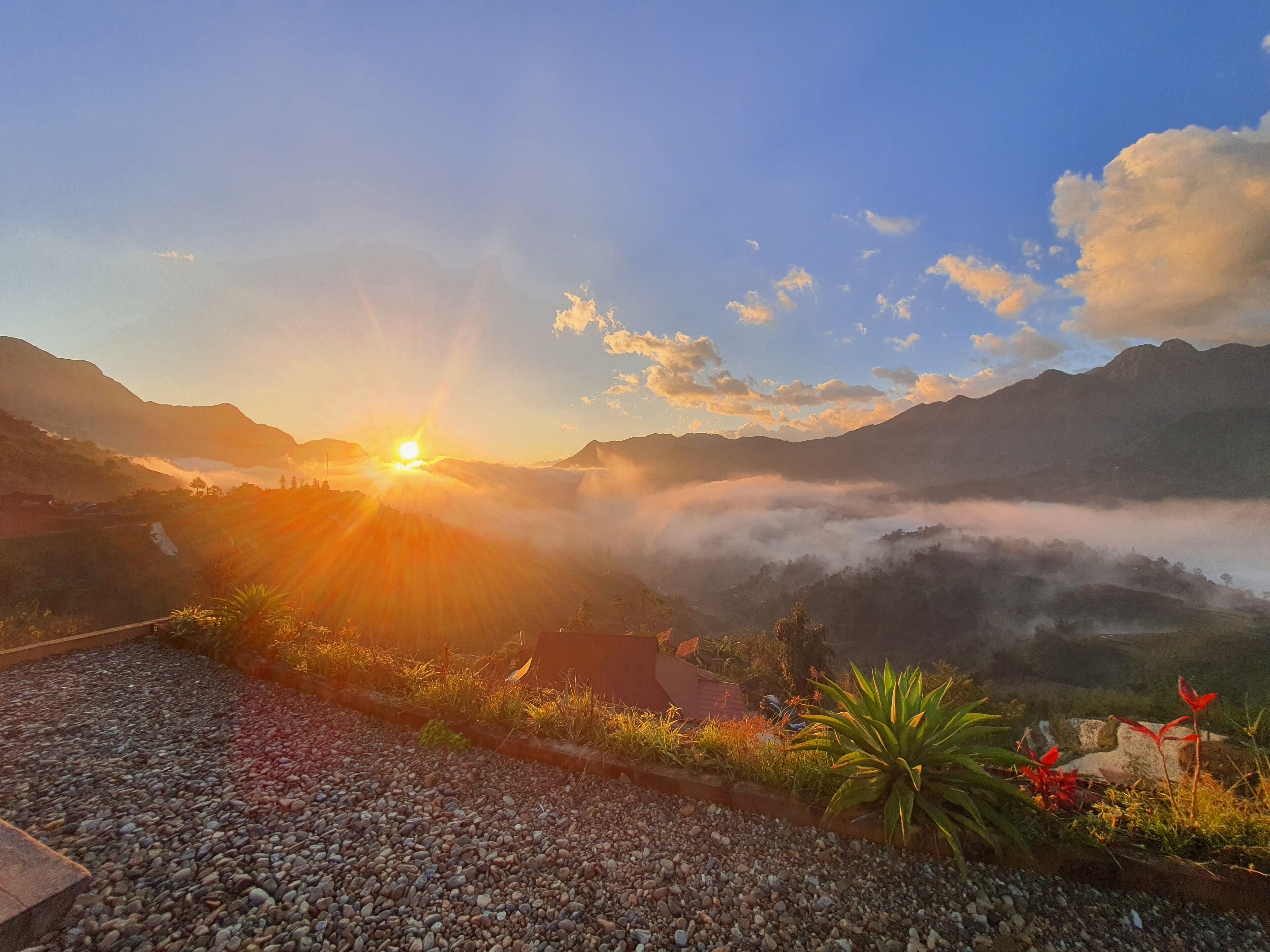 A mountainous landscape with a sunrise, a clear sky, and a view of the valley below.