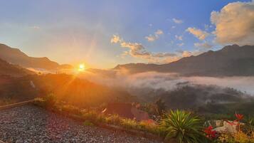 A mountainous landscape with a sunrise, a clear sky, and a view of the valley below.