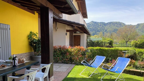 Eine Terrasse mit Esstisch, zwei Lounge-Stühlen und einem gepflegten Rasen.