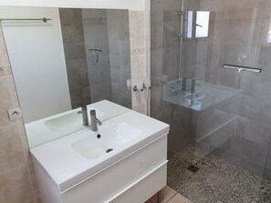 Uma casa de banho moderna com lavatório branco, cabine de duche com vidro e espelho sobre o lavatório.