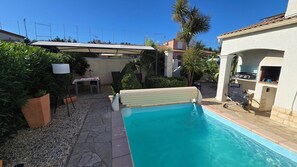 Um quintal com piscina, móveis de pátio, área de churrasco e um espaço de estar coberto.