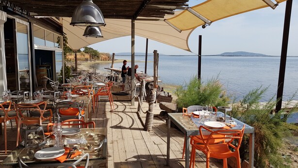 An outdoor dining area with tables and chairs, overlooking a body of water. - Stylish house with medit. Garden, AC, barbecue, private + heated. Pool and W-Box (Portiragnes)
