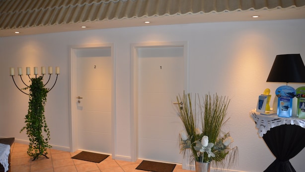 A hotel lobby with two doors, a reception desk, a plant, and a table with items on it.