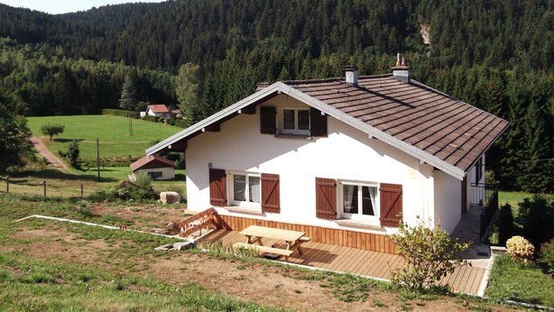 A white house with a sloped roof, wooden shutters, and a wooden deck. - Le Moulin de Bouvacôte (Le Tholy)