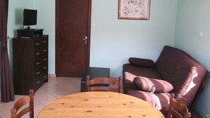 A living room with a wooden table, a brown sofa, a TV on a cabinet, and a door. - Le Moulin de Bouvacôte (Le Tholy)