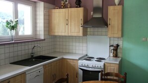 A kitchen with wooden cabinets, a white stove, a sink, and a window with a plant. - Le Moulin de Bouvacôte (Le Tholy)