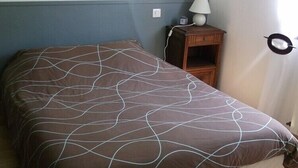 A single bed with a patterned bedspread, a bedside table with a lamp, and a wall-mounted hat. - Le Moulin de Bouvacôte (Le Tholy)