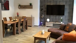 Una sala de estar moderna con comedor, un televisor de pantalla plana montado en una pared texturizada y una mesa de centro de madera.
