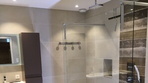 Un baño moderno con ducha acristalada, tocador con espejo y suelo de madera.