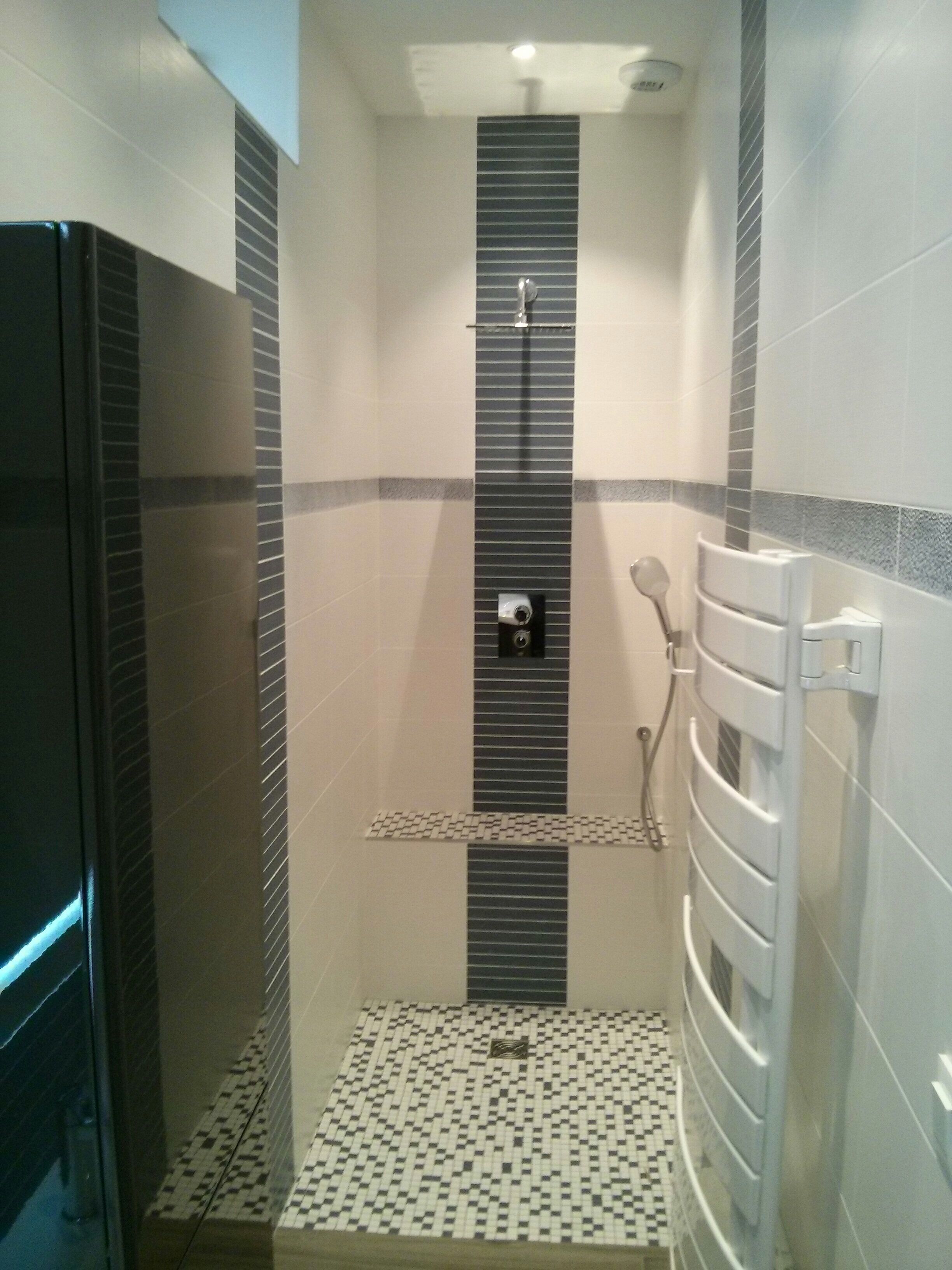 A modern shower with a black and white tiled floor, a vertical black and white striped wall, and a white towel rack.