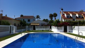 A swimming pool with a clear blue water, surrounded by a white fence, and adjacent to a building with a red-tiled roof.