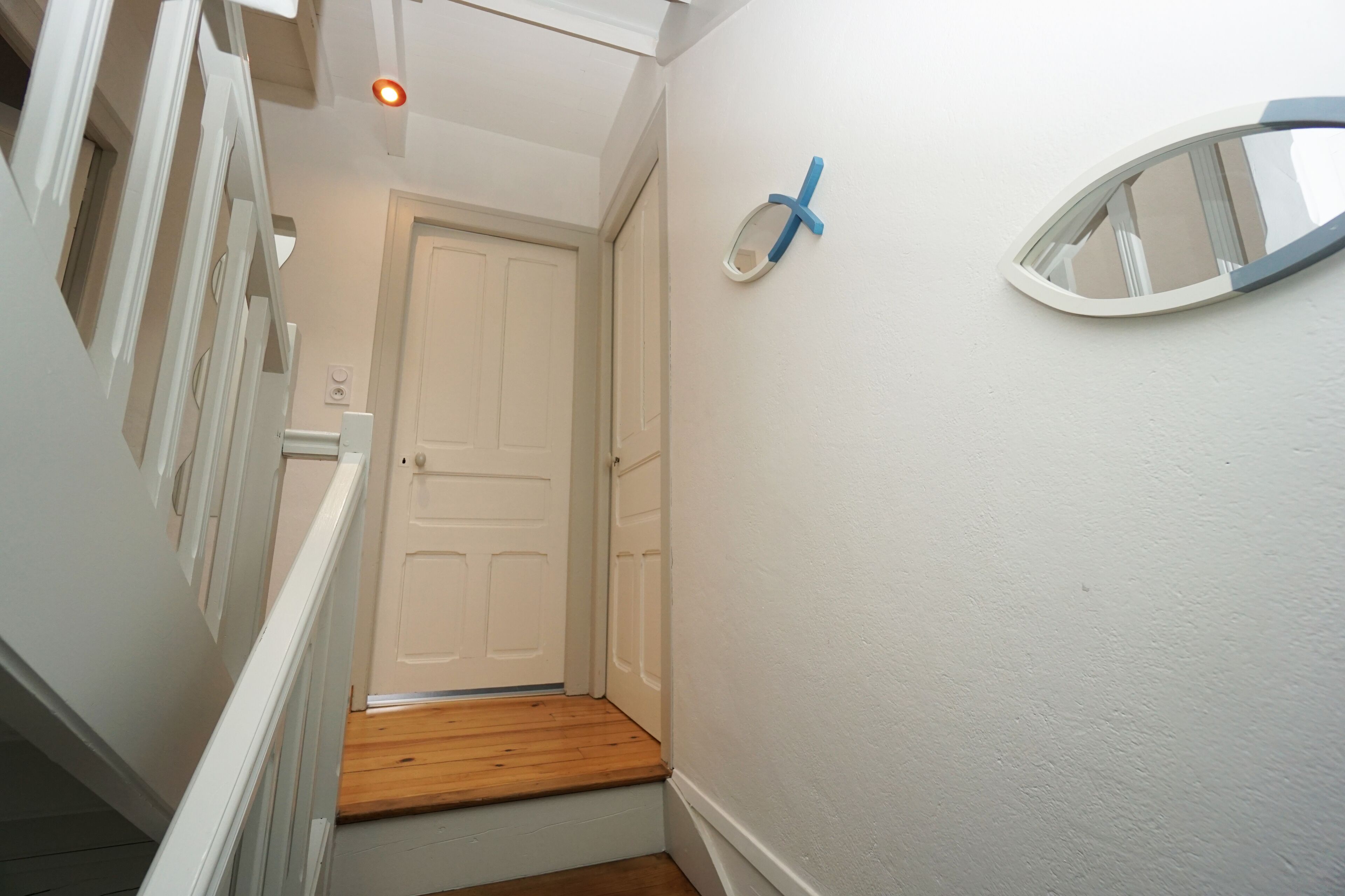 Un couloir étroit avec un escalier en bois menant à une porte blanche.