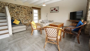A cozy living room with a stone wall, a sofa, a coffee table, wicker chairs, and a TV. - Cottage on the Crozon peninsula (Lanvéoc)