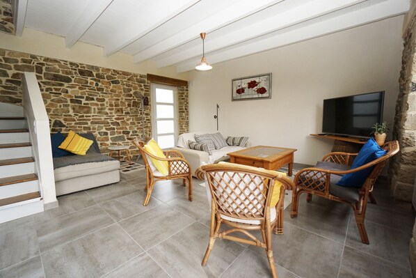 A cozy living room with a stone wall, a sofa, a coffee table, wicker chairs, and a TV.