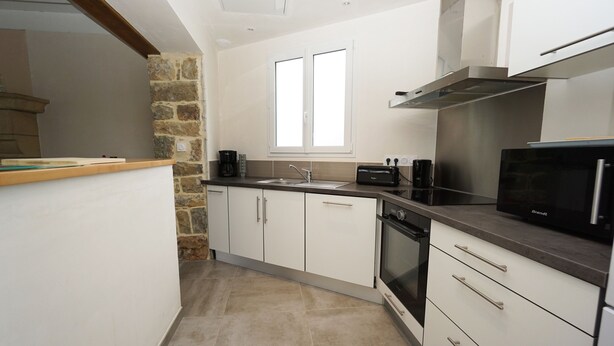A modern kitchen with white cabinets, a stone accent wall, a built-in oven, and a window above the sink. - Cottage on the Crozon peninsula (Lanvéoc)