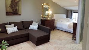Un dormitorio con cama, un sofá marrón, cómoda, espejo y un cuadro en la pared.