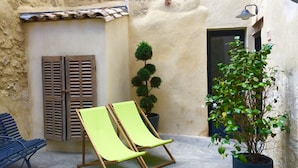 Un patio con un banco, dos sillas, una planta en maceta y una puerta.