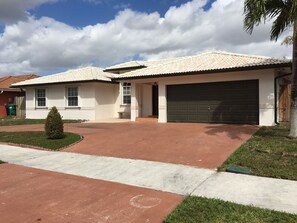 A two-story house with a tiled roof, a garage, and a small front yard with a tree.