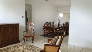 Un coin repas comprenant une table à manger en bois, des chaises assorties, un tapis à motifs et un canapé agrémenté d’un coussin à rayures.