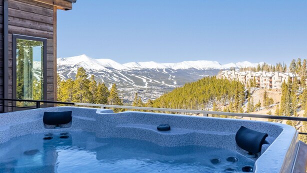 A hot tub with a mountain view, wooden cabin, and a clear sky.