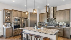 A modern kitchen with stainless steel appliances, a granite island with bar stools, and pendant lighting.