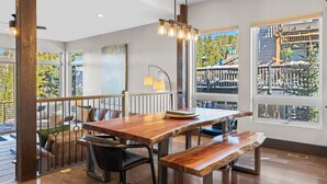 A dining area with a wooden table, benches, and a view of a balcony with outdoor furniture.