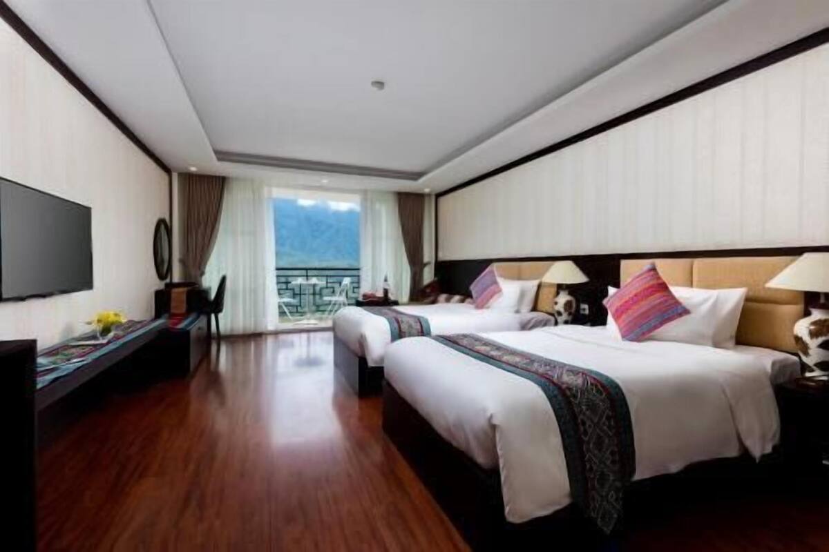 A hotel room with two beds, a TV, a desk, and a balcony with a view.