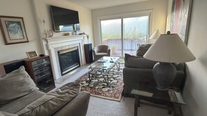 Una sala de estar con chimenea, un sofá, una mesa de centro y un televisor sobre la chimenea.