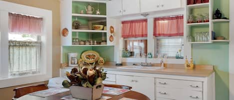 Una cocina con armarios blancos, una mesa de comedor de madera con individuales, y un ventilador de techo.