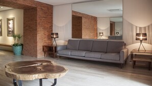 Een moderne woonkamer met een grijze bank, een houten salontafel en een grote spiegel.