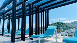 Een dakterras met blauwe lounge stoelen en een overdekte glazen constructie.