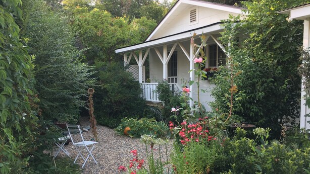 A house with a covered porch, surrounded by dense greenery and a gravel path. - DOWNTOWN MURPHYS, HALF BLOCK TO MAIN ST (Murphys)