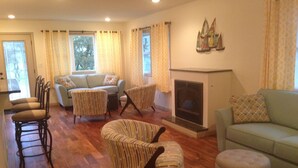 Ein geräumiges Wohnzimmer mit Kamin, einer Couch, gestreiften Sesseln und einem Essbereich mit Stühlen.