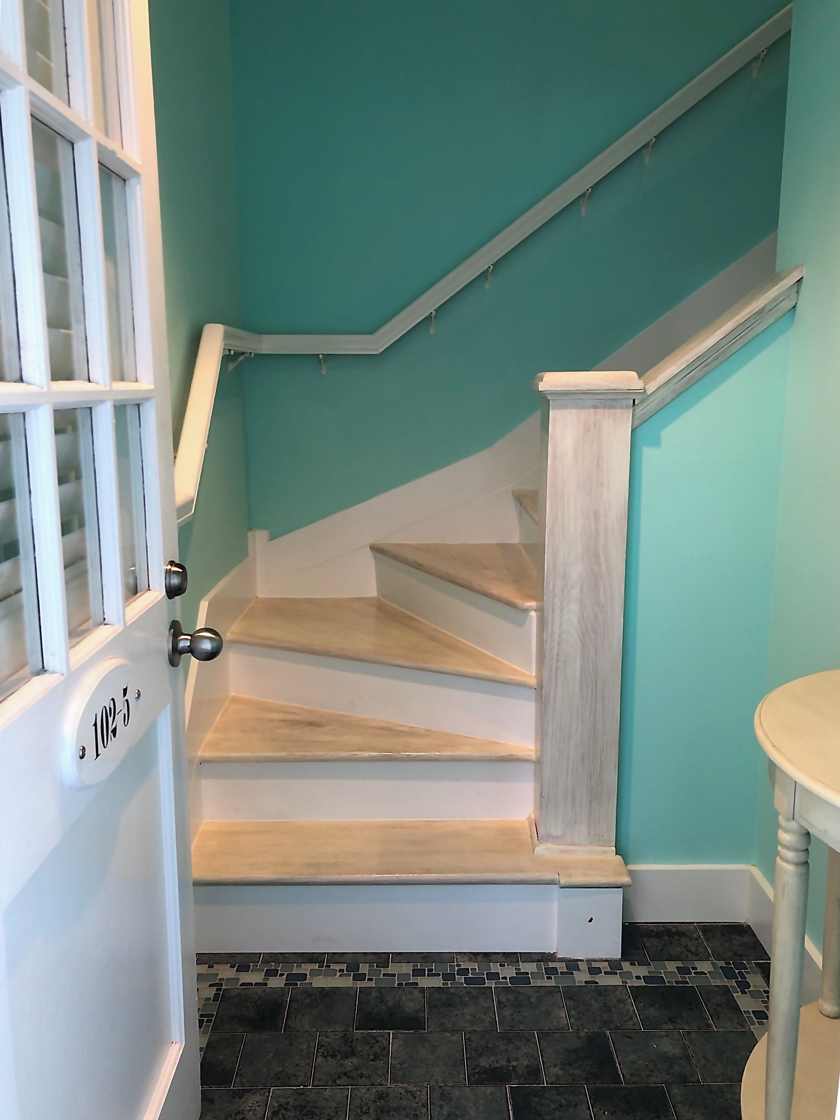 Eine Treppe mit heller Holzvertäfelung, einem weißen Geländer und einer türkisblauen Wand.