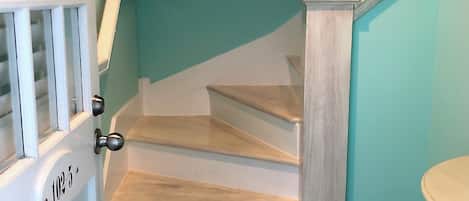 Una escalera con acabado en madera clara, barandilla blanca y pared color aguamarina.