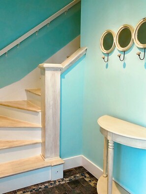 Un escalier avec des marches blanches et une rampe en bois, menant à une pièce dont un mur est peint en bleu clair et qui contient une coiffeuse blanche avec un miroir.